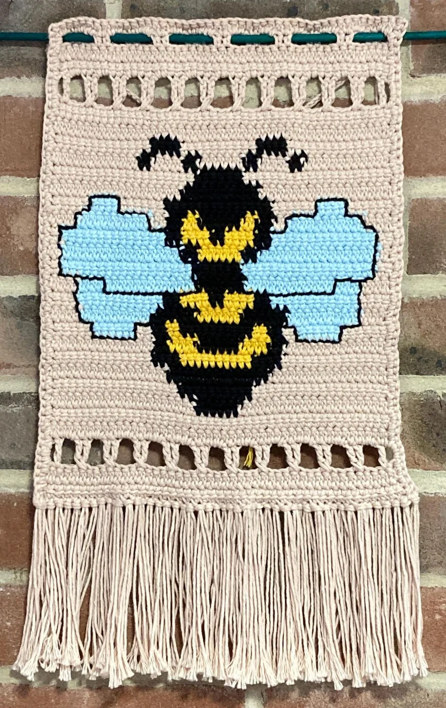 Bumblebee tapestry crochet wall hanging against a brick wall